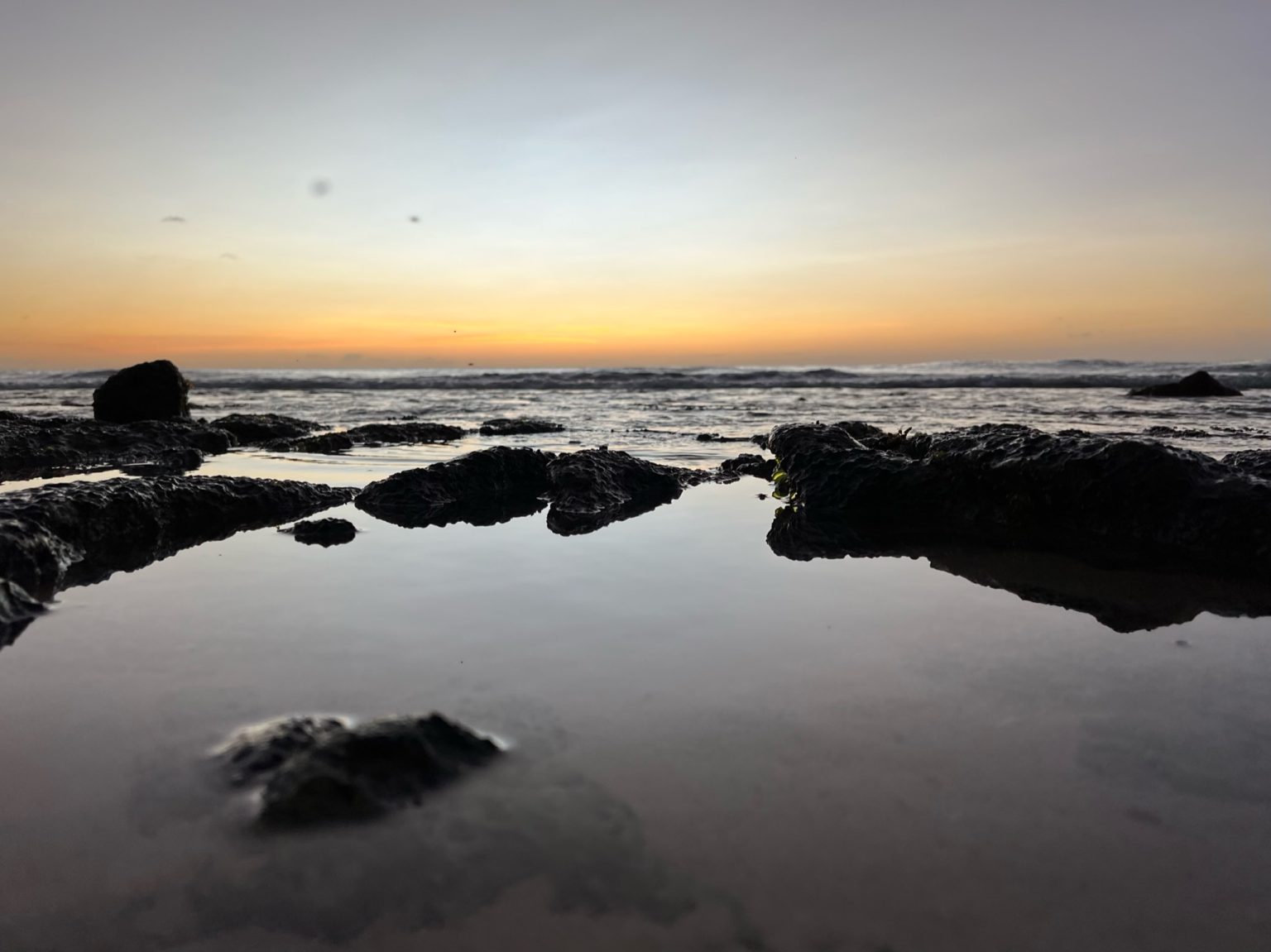 Sunset over a rocky shoreline, the sky glowing amber above the sea.